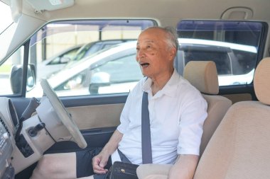 Beyaz gömlekli ve siyah kravatlı bir adam arabada oturuyor. Gülümsüyor ve mutlu.