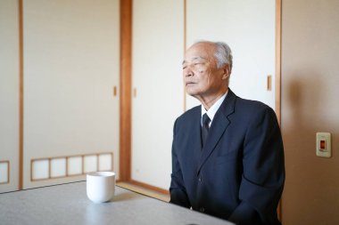 Takım elbiseli bir adam bir fincan kahveyle masada oturuyor. Rahat bir ruh hali içinde, muhtemelen yalnızlık ya da tefekkür anının tadını çıkarıyor. Sakinlik ve sükunet kavramı