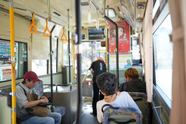 Otobüs insanlarla dolu, bazıları maske takıyor. Otobüs sarı ve kırmızı çizgili.