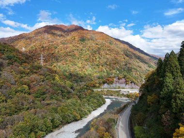 İçinden nehir akan bir dağ sırası. Ağaçlar sonbahar yapraklarıyla kaplıdır. Gökyüzü açık ve mavi
