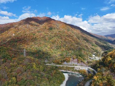 İçinden geçen dolambaçlı bir yolu olan bir dağ sırası. Yol ağaçlarla çevrilidir ve dağlar sonbahar yapraklarıyla kaplıdır. Huzurlu ve huzurlu bir sahne.