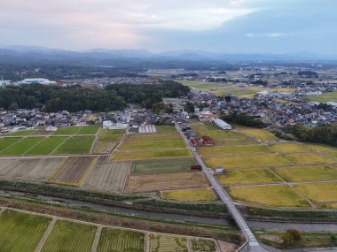 Kırsal bir bölge ve içinden bir nehir geçiyor. Gökyüzü bulutlu ve güneş batıyor.