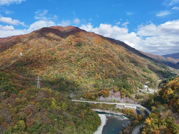 İçinden geçen dolambaçlı bir yolu olan bir dağ sırası. Yol ağaçlarla çevrilidir ve dağlar sonbahar yapraklarıyla kaplıdır. Huzurlu ve huzurlu bir sahne.