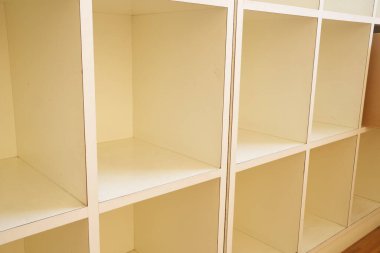 Beyaz bir dolabın boş rafları görünür, üzerinde hiçbir şey yoktur. Dolap beyaz ahşaptan yapılmıştır ve tertemiz, minimalist bir görünüme sahiptir.