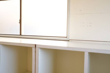 Üstünde pencere olan beyaz bir dolap. Pencere açık ve dolap boş. Dolap beyaz duvarlı bir odada.