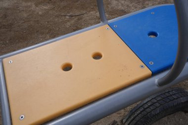 Mavi ve sarı koltuklu bir bank. Koltuk plastikten yapılmış ve üzerinde iki delik var.