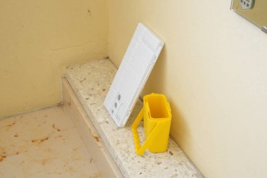 Sarı kapaklı beyaz bir kutu sarı bir kovanın yanında bir tezgahın üzerinde. Olay yeri dağınık ve dağınık.