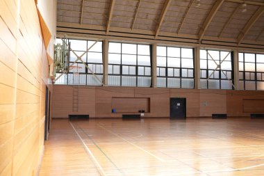 Basketbol potası ve bank olan bir spor salonu. Oda boş ve duvarlar tahtadan yapılmış.