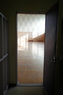 Bir spor salonunda bir kapı açıktır. Oda boş ve zemin tahtadan yapılmış.