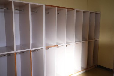 İçinde metal kancalar olan bir sıra beyaz dolap. Dolaplar boş. Oda aydınlık ve temiz.