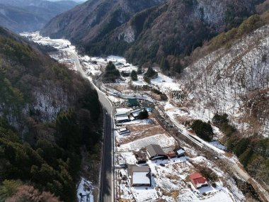 Karlı bir dağ sırasının içinden geçen bir yol. Yol boş ve evler küçük.
