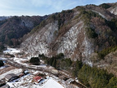 Önünde küçük bir köy olan karlı bir dağ sırası. Köy ağaçlarla çevrili ve dağlar karla kaplı. Sahnenin huzurlu ve huzurlu bir havası var.