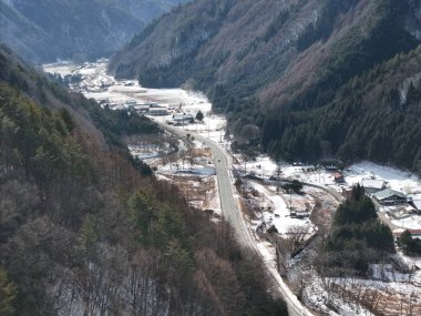 İçinden yol geçen karlı bir dağ. Yol boş ve evler küçük.