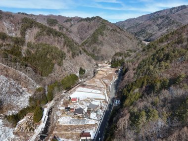 İçinden yol geçen bir dağ sırası. Yol boş ve evler de küçük. Gökyüzü açık ve güneş parlıyor.