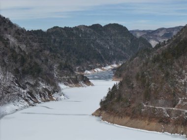 İçinden bir nehir akan karlı bir dağ sırası. Nehir donmuş ve ağaçlar karla kaplanmış.