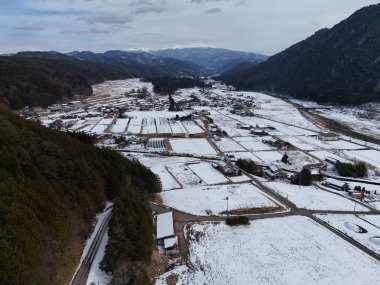 Arkasında küçük bir kasaba olan karlı bir manzara. Gökyüzü bulutlu ve kar zemini kaplıyor.