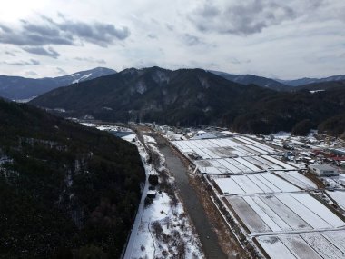 Bir kasabanın arka planında karlı bir dağ sırası görülebilir. Kasaba bir nehir ve bir kar tarlası ile çevrilidir. Gökyüzü bulutlu ve görüntünün genel havası sakin ve huzurlu.