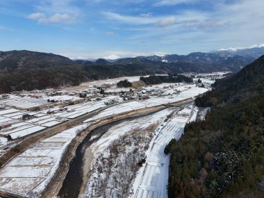 İçinden bir nehir akan karlı bir manzara. Sahne huzurlu ve huzurlu. Karla kaplı zemin ve arkadaki dağlar bir sakinlik ve sükunet hissi yaratıyor.