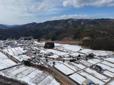 Uzakta küçük bir kasabası olan karlı bir manzara. Gökyüzü bulutlu ve arka planda dağlar var