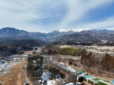 Önünde bir köprü bulunan bir dağ sırası uzaktan görülebilir. Gökyüzü açık ve mavi ve dağlar karla kaplı. Huzurlu ve huzurlu bir sahne.