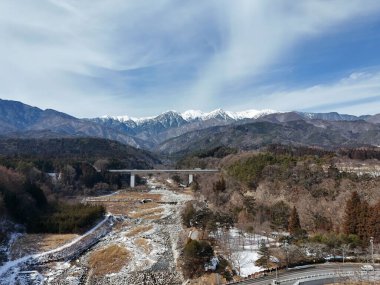 Önünde bir köprü bulunan bir dağ sırası uzaktan görülebilir. Gökyüzü açık ve mavi ve dağlar karla kaplı. Huzurlu ve huzurlu bir sahne.