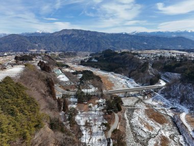 Ortasında köprü olan karlı bir dağ sırası. Köprü bir nehrin üzerinde ve dağlar da arka planda.