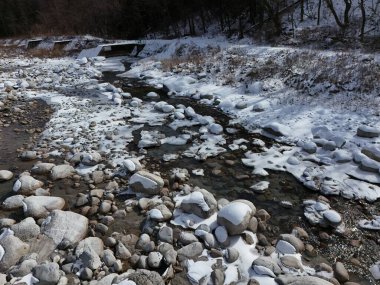 Bir nehir kayalar ve karla kaplı. Kayalar nehrin dört bir yanına dağıldı ve karlar kıyılara yığıldı. Huzurlu ve huzurlu bir sahne.