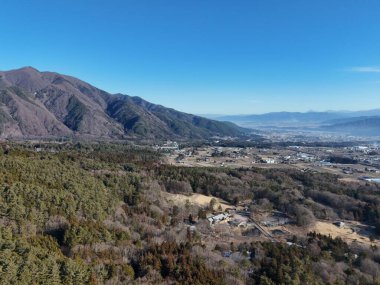 Uzakta bir şehir olan bir dağ sırası. Gökyüzü açık ve mavi. Şehir küçük ve kırsal bir hissi var.