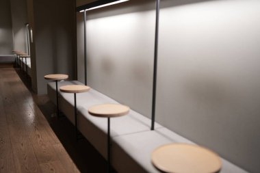 Yuvarlak koltuklu ahşap banklar bir duvara karşı dizilmiştir. Banklar boş ve oda loş bir şekilde aydınlatılmış.