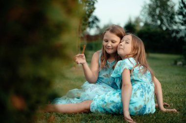 Siyah saçlı, mavi elbiseli iki tatlı kız güneşli bir yaz gününde dışarıda çiçek topluyor. Yaz tatili.