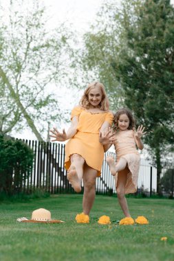 Elbiseli anne ve kızı çimenlikteki yazlık evde dinleniyor ve keyif alıyorlar. Yaz tatili. Doğa ve temiz hava. Peyzaj ve tasarım.