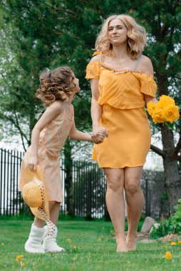 Elbiseli anne ve kızı çimenlikteki yazlık evde dinleniyor ve keyif alıyorlar. Yaz tatili. Doğa ve temiz hava. Peyzaj ve tasarım.