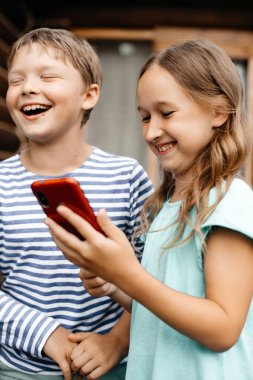 Erkek ve kız akıllı telefonda oyun oynayıp gülüyorlar. Yaz tatili. Tasasız çocukluk. Mutluluk ve eğlence konsepti.