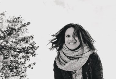 Parktaki bulutların ve ağaçların arkasında gülümseyen bir kızın siyah beyaz fotoğrafı..