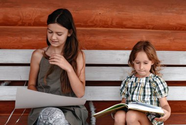 İki kız, ahşap bir evin yakınındaki boş bir bankta otururken çizim yapmakla meşgul. Sanat ve çizim kavramı.