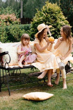 Üç küçük kız salıncağa biniyor ve yazın köyde eğleniyorlar. Şapkalı bir çocuk. Yaz tatili. Çocuk stili ve moda kavramı. Tonlama.