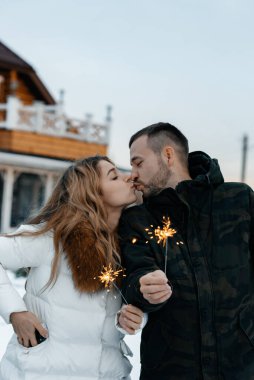 Birbirine aşık bir çift, ellerinde kıvılcımlar tutarak birbirlerini kucaklıyor. Karlı bir gün. - Evet. Yılbaşı tatilleri. Mutluluk ve aşk kavramı.