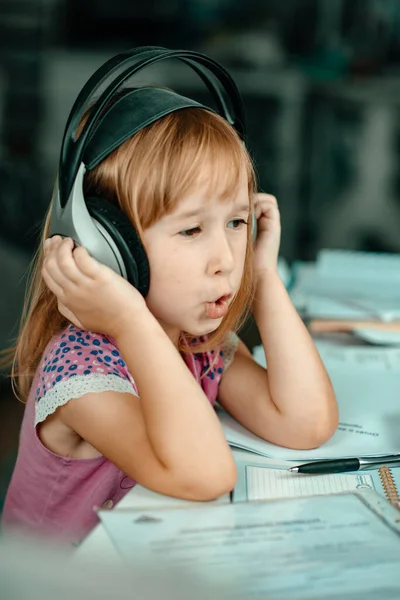 Little girl listens to music in headphones. Home schooling. Technology and music concept. The child learns something new.