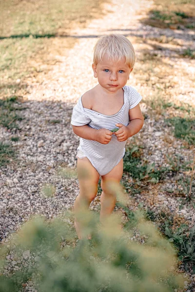 A little blond boy in a white bodysuit walks barefoot down the street. The concept of happiness and positivity. Carefree childhood and summer.