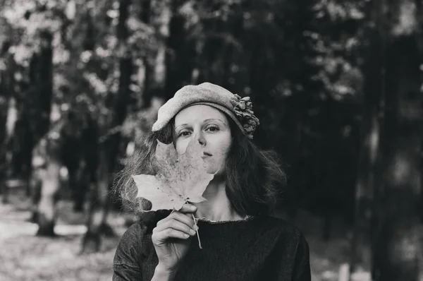 頭にベレー帽をかぶった女の子が秋の公園を歩いている 彼女の手に葉を持つ女の子 地面に落ちた紅葉 — ストック写真