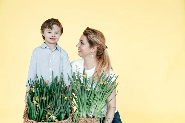 A boy with Down Syndrome and mom holds flowers in her hands, in the background is a yellow background. The concept of care for the disabled. Family story. Mothers Day. Coppy Space. Toning.