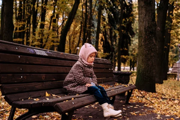 Грустная Маленькая Девочка Коричневом Пальто Сидит Одна Скамейке Осеннем Парке — стоковое фото