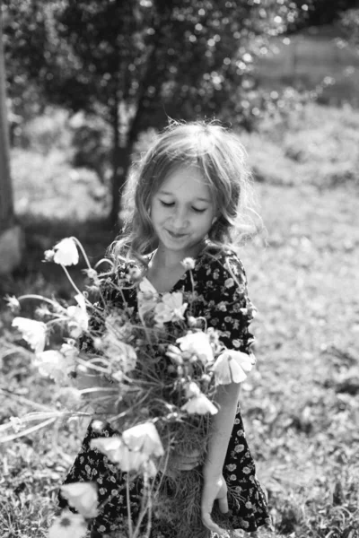 一张黑白照片 照片上的一个黑发小女孩穿着一件黑色连衣裙 手里拿着一束鲜花 幸福与宁静的概念 无忧无虑的童年 — 图库照片