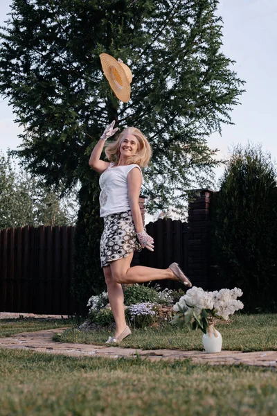 笑逐颜开的金发姑娘把草帽扔了上来 背靠着木头 夏天阳光充足 快乐与喜悦的概念 花瓶里的丁香 — 图库照片