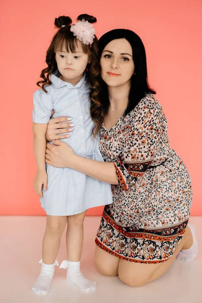 ドレスを着たママは娘をピンクの背景にダウン症候群で抱きかかえています 障害者介護の概念 母の日 コピースペース トーニング — ストック写真