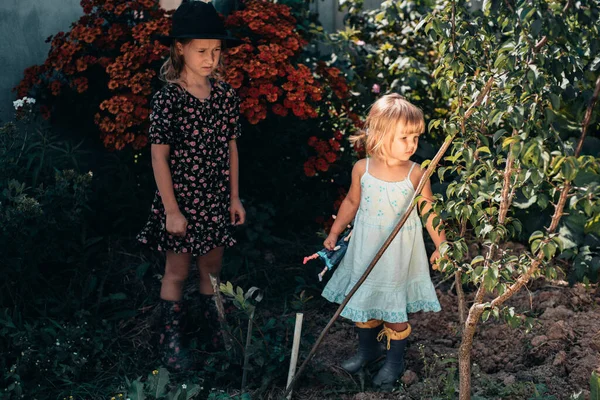两个戴着衣服和帽子的小女孩在达查花园散步 鲜花盛开 无忧无虑的童年暑假 幸福与宁静的概念 — 图库照片
