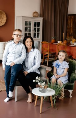 Gömlek giyen koyu renk saçlı bir kız, bir koltukta oğlunun ve kızının yanında oturur. Aile fotoğrafı. Mutluluk ve ilgi kavramı. Anneler Günü.