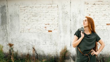 Koyu yeşil elbiseli, uzun saçlı güzel bir kız eski bir tuğla binanın arka planında. Kırsal.