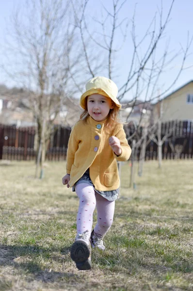 一个戴着黄色巴拿马帽和黄色外套的小女孩跑到公园外面去了 温暖的晴天春天来了 — 图库照片