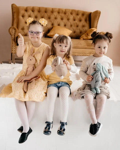 ドレスを着た女の子たちがおもちゃを手にスタジオに座っている ダウンは頑固だ 特別なニーズを持つ子供のためのヘルプコンセプト — ストック写真